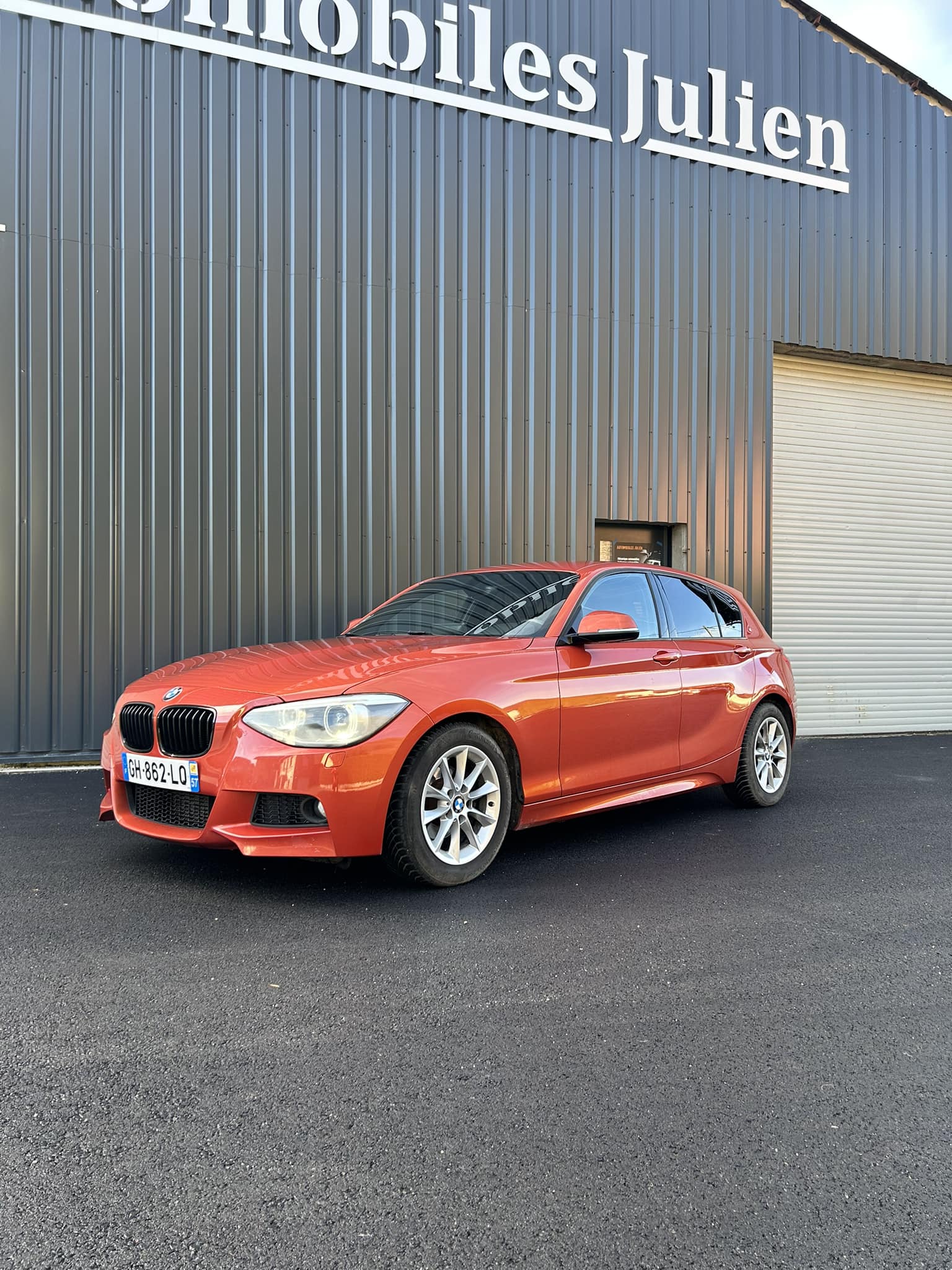 BMW Série 1 orange devant le garage